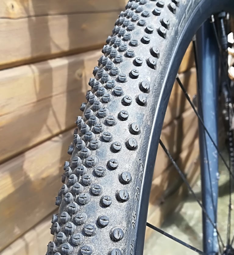 Close view of the knobbly Schwalbe G-One Bite tread on a gravel bike wheel, leaning against a wooden wall.