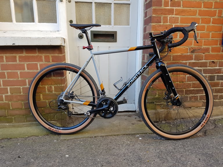 Side view of the black and grey Bombtrack Audax with Hunt wheels, against a brick wall and white door.
