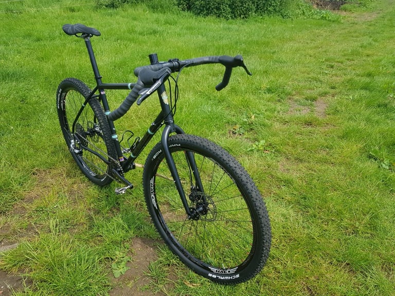 Light Blue Darwin One By MT in matt black with drop bars and wide Schwalbe tyres, seen from the front on grass.