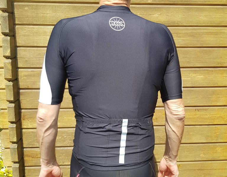 Back of the black Le Col HC Clima jersey, with a reflective stripe up the centre pocket and a round logo.