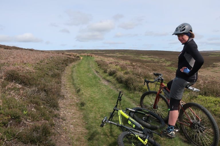 Debs pauses beside her Salsa Deadwood on a grassy moorland trail, with the organisers' e-bike lying in the grass.