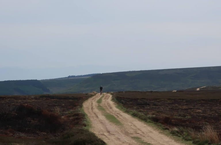 Lone rider on a wide gravel track crossing heather moorland on the Yorkshire True Grit course in the North York Moors.