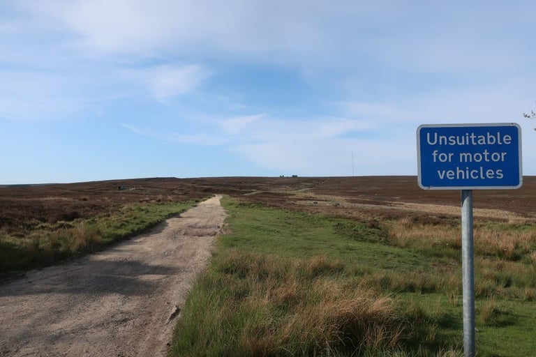 Blue 'Unsuitable for motor vehicles' sign beside a gravel track over heather moor on the Yorkshire True Grit route.