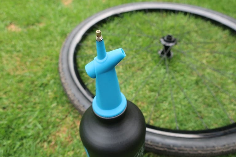 Blue MilKit Booster head on its bottle beside a Halo Vapour GXC wheel with a freshly seated Panaracer Gravel King tyre.