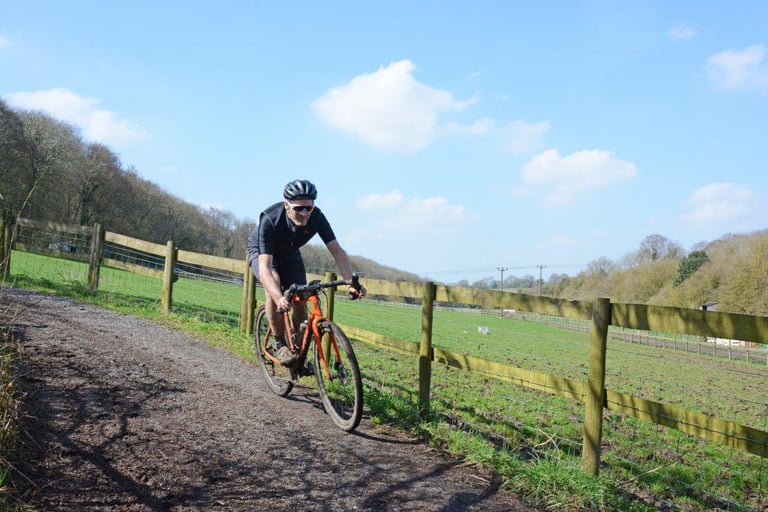 James Deane corners his orange Mason Bokeh gravel bike on a track beside a fenced field in Hertfordshire.