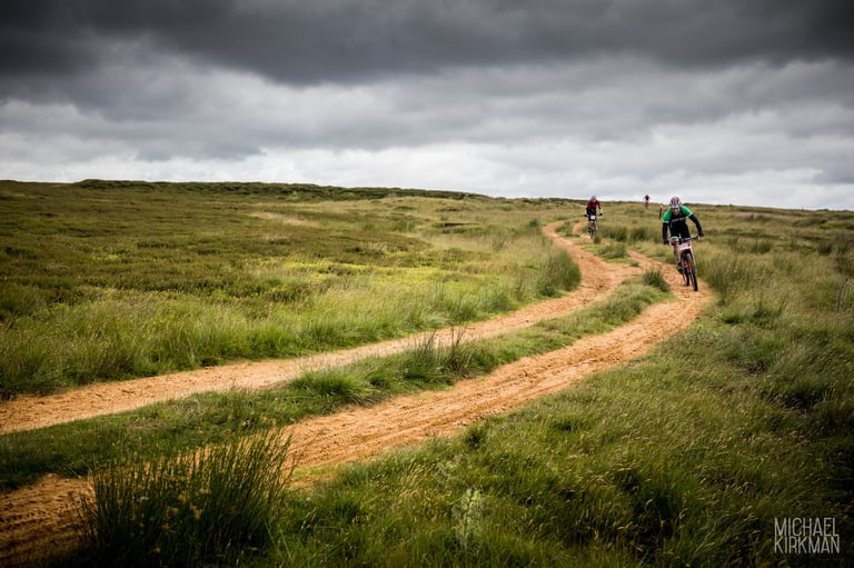 Yorkshire True Grit riders follow a winding sandy track across open moorland under dark clouds.