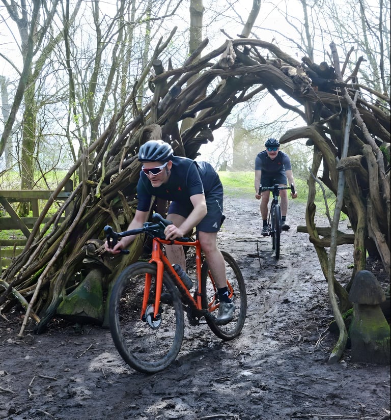 James Deane and Nigel Leech ride under an arch of woven branches on a muddy Chilterns woodland trail.