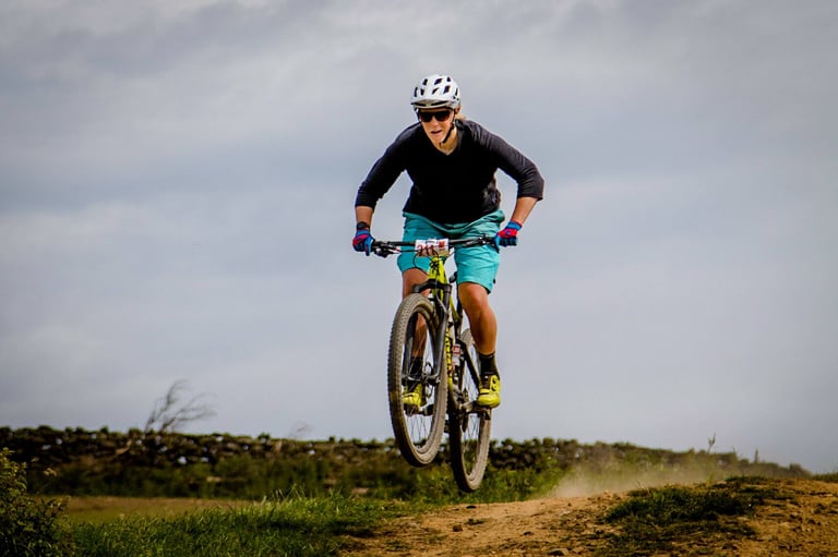 Rider in teal shorts lifts the front wheel of a mountain bike off a grassy bank at Yorkshire True Grit.