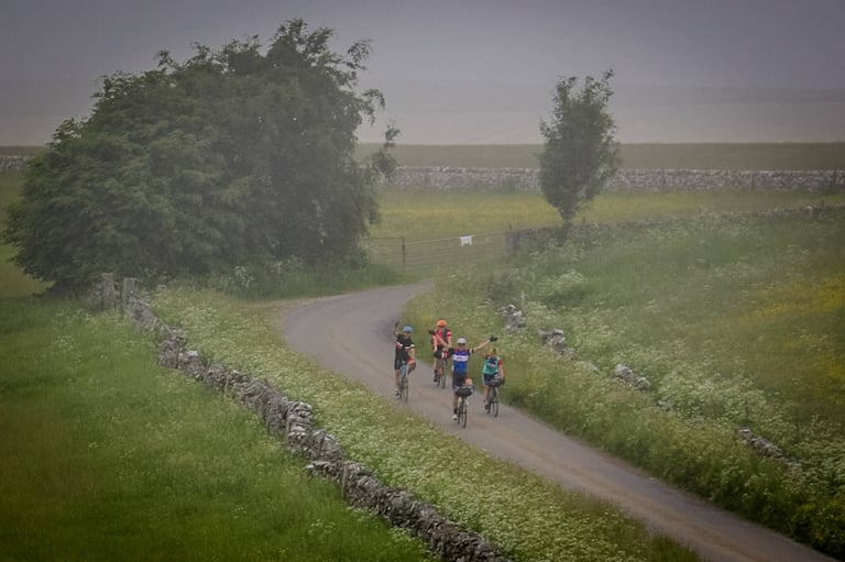 Group of riders wave as they head back towards Buxton along a misty walled lane lined with wildflowers.