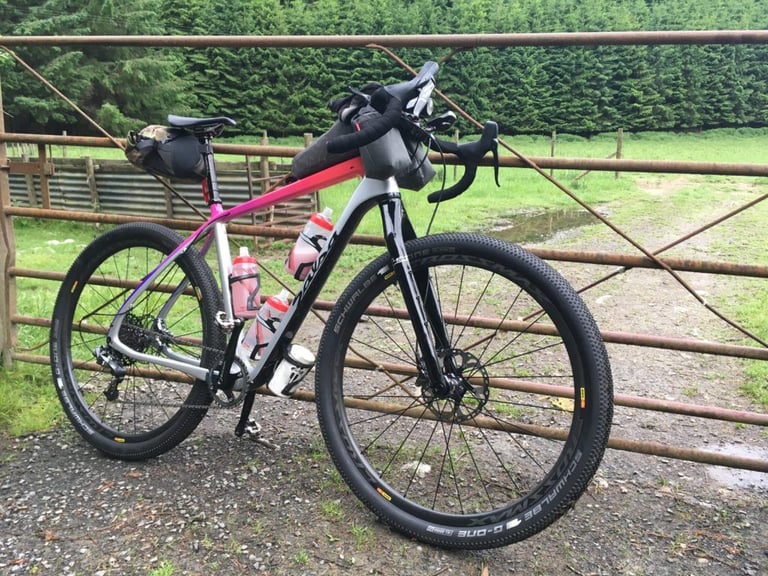 Salsa Cutthroat gravel bike with Schwalbe G-One tyres and bikepacking bags, leaning on a farm gate before the TINAT 400.
