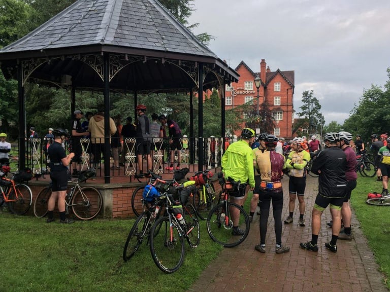 Riders and loaded bikes gather at a bandstand to collect brevet cards before the TINAT 400 start in Llandrindod Wells.