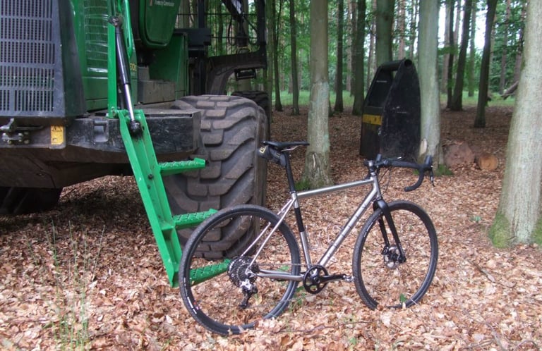 Reilly Gradient titanium bike beside a green Forestry Commission machine in woodland covered in fallen leaves.