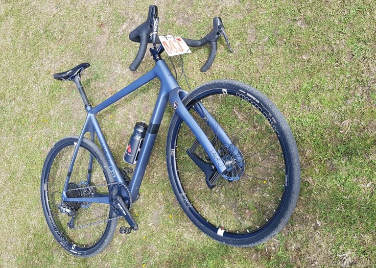 Lauf True Grit lying on the grass with a race number board on the bars at Yorkshire True Grit.
