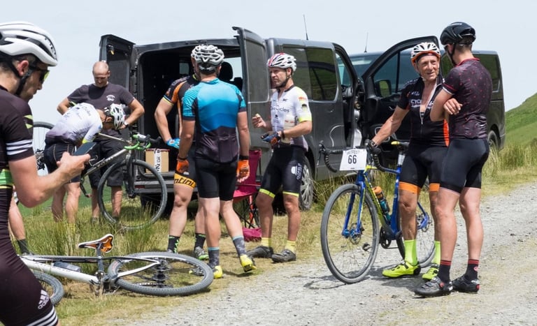 Riders chat beside an open van and parked bikes at a gravel track stop during Gritfest.