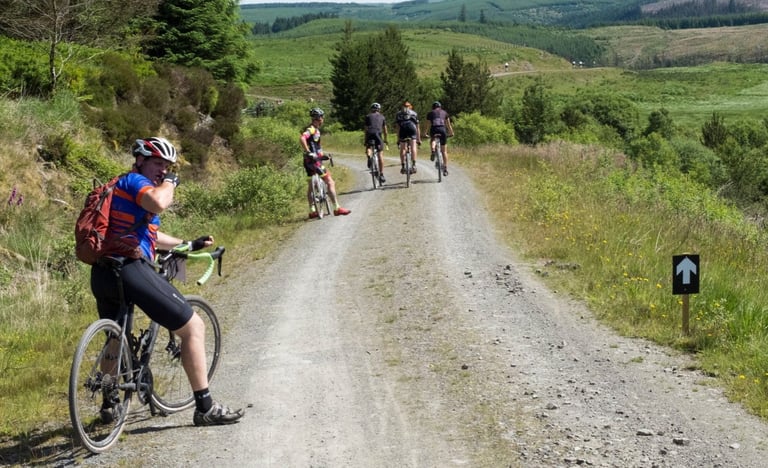 Gritfest rider looks back on a gravel climb as others ride on, with a course arrow sign beside the track.