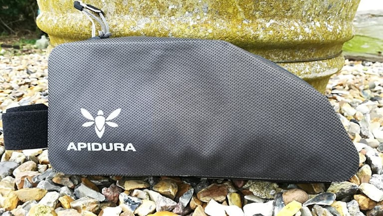 Side view of the 1L Apidura Expedition top tube bag in grey waterproof laminate, with zip pull, on gravel.