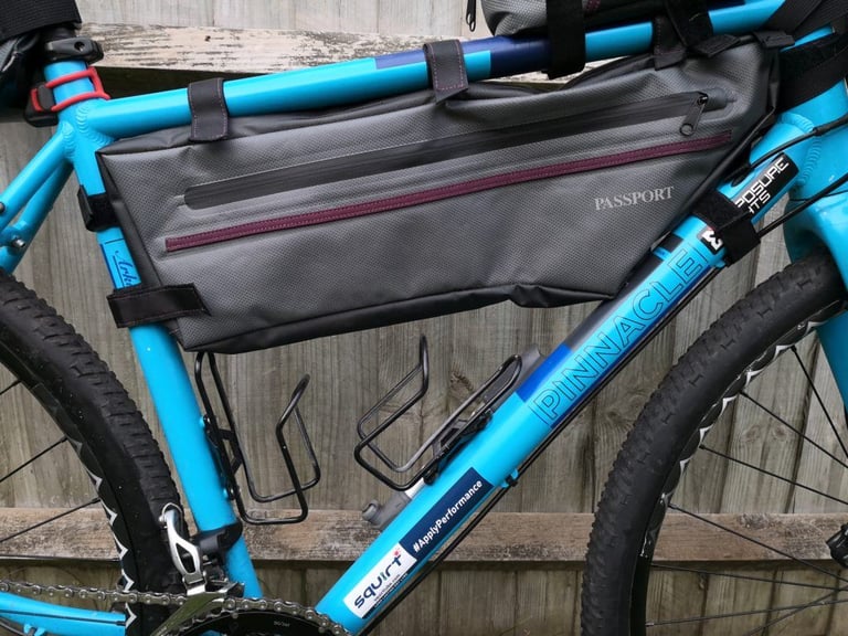 Passport frame bag on a blue Pinnacle bike with standard wire bottle cages squeezed beneath it.