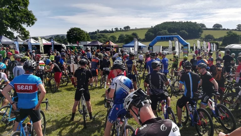 Riders gather on the grass at the Gritfest 2018 start line beneath the inflatable arch, trade tents behind.