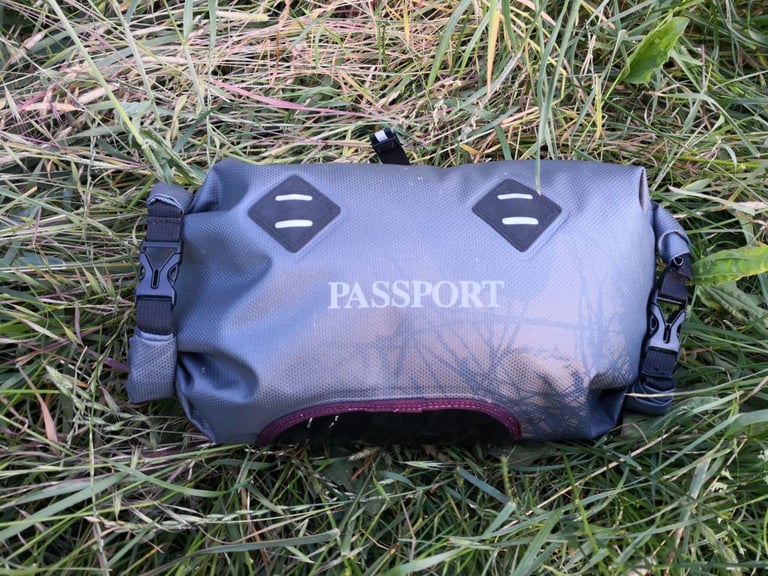 Front of the Passport handlebar bag with logo, reflective patches and side buckles on grass.