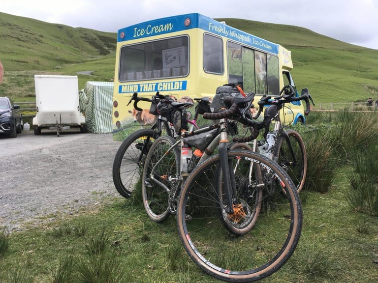 Three gravel bikes with bikepacking bags parked on the grass beside an ice cream van during the TINAT 400km Audax.