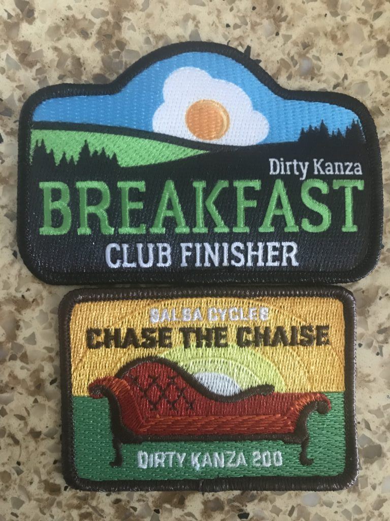 Dirty Kanza Breakfast Club Finisher patch above a Salsa Cycles Chase the Chaise Dirty Kanza 200 patch on a worktop.