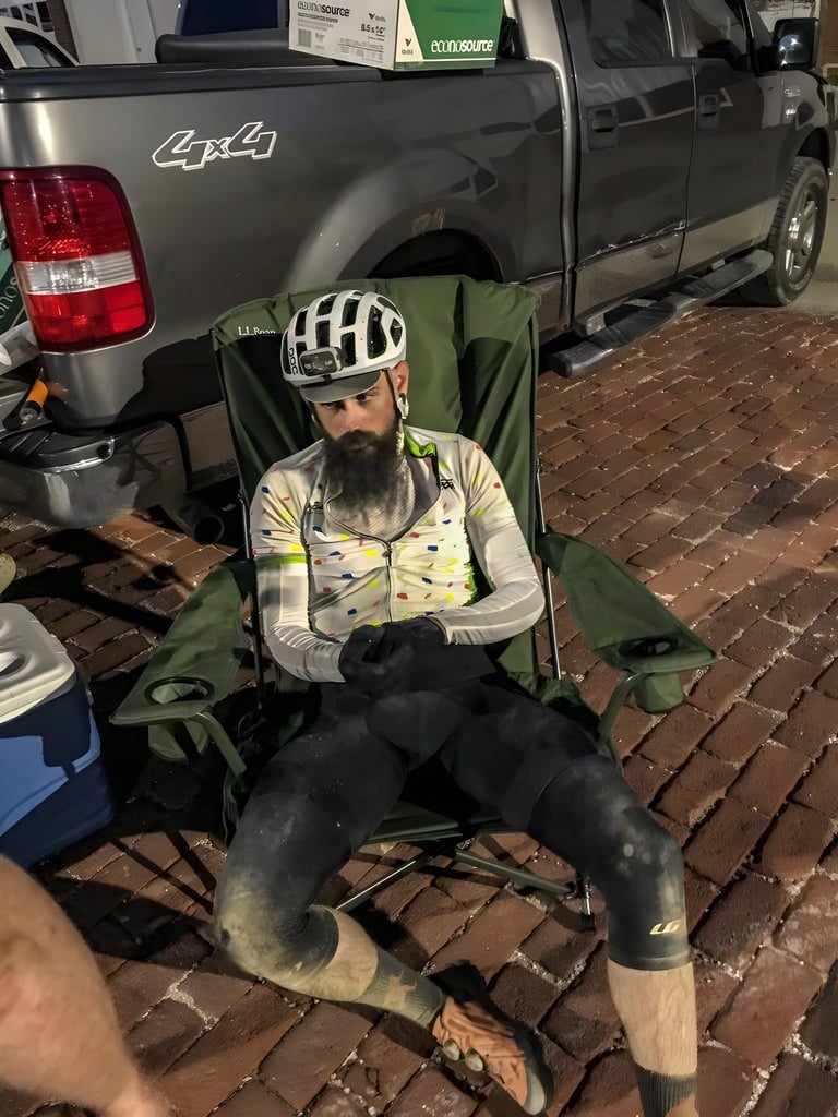 Exhausted David Markman in helmet and dust-stained kit slumps in a camping chair by a pickup after the Dirty Kanza 200.