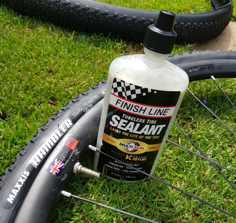 Finish Line tubeless sealant bottle propped against a Maxxis Rambler 700x40c tyre and wheel on grass before setup.