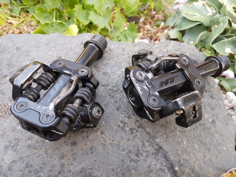 Pair of black HT Leopard M1 pedals after 800 miles, with minor scuffs on the bodies, resting on a rock.