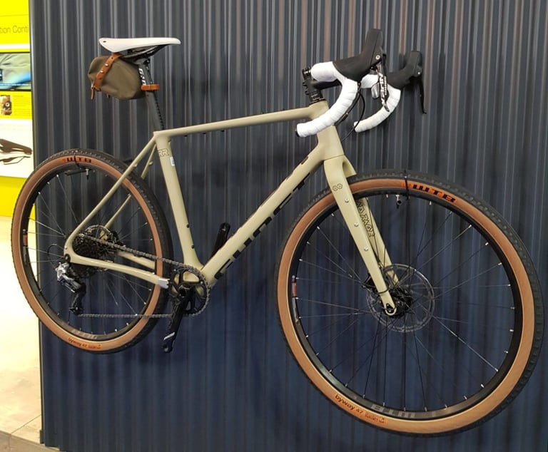 Ghost Road Rage Endless in sage green with white bar tape, WTB Byway tanwall tyres and saddle bag, hung on a wall.