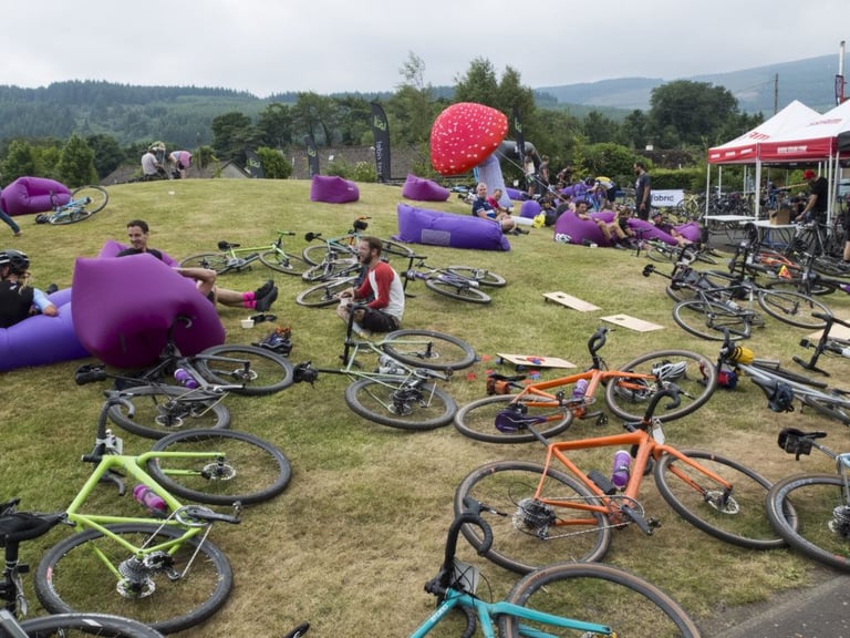 Gravel bikes lie on the grass among purple inflatable loungers and sponsor tents at the Grinduro bike park on Arran.