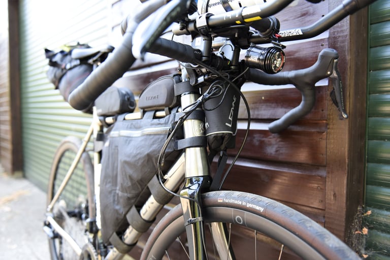Kinesis GTD leant against a wooden wall, loaded with Lezyne frame bag, stem bag, saddle pack and a front light.
