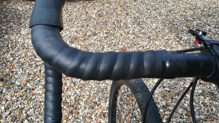 Dusty Genetic silicone tape on a gravel bike's drops and tops, with a knobbly tyre on gravel behind.
