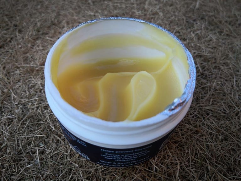 Open tub of Squirt Barrier Balm showing the thick, pale yellow balm inside, with its foil seal peeled back.