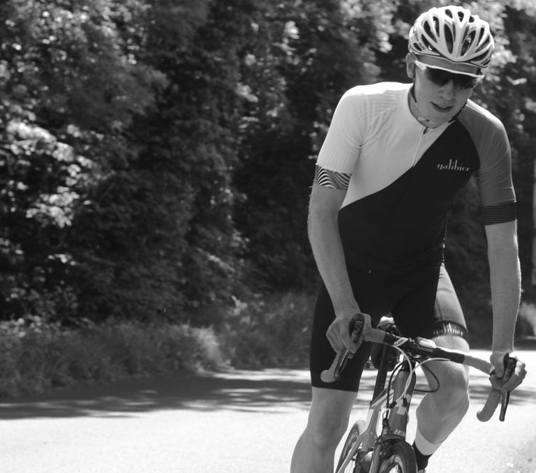 Black and white shot of a rider in Galibier Peloton bib shorts and a Galibier jersey on a tree-lined road.