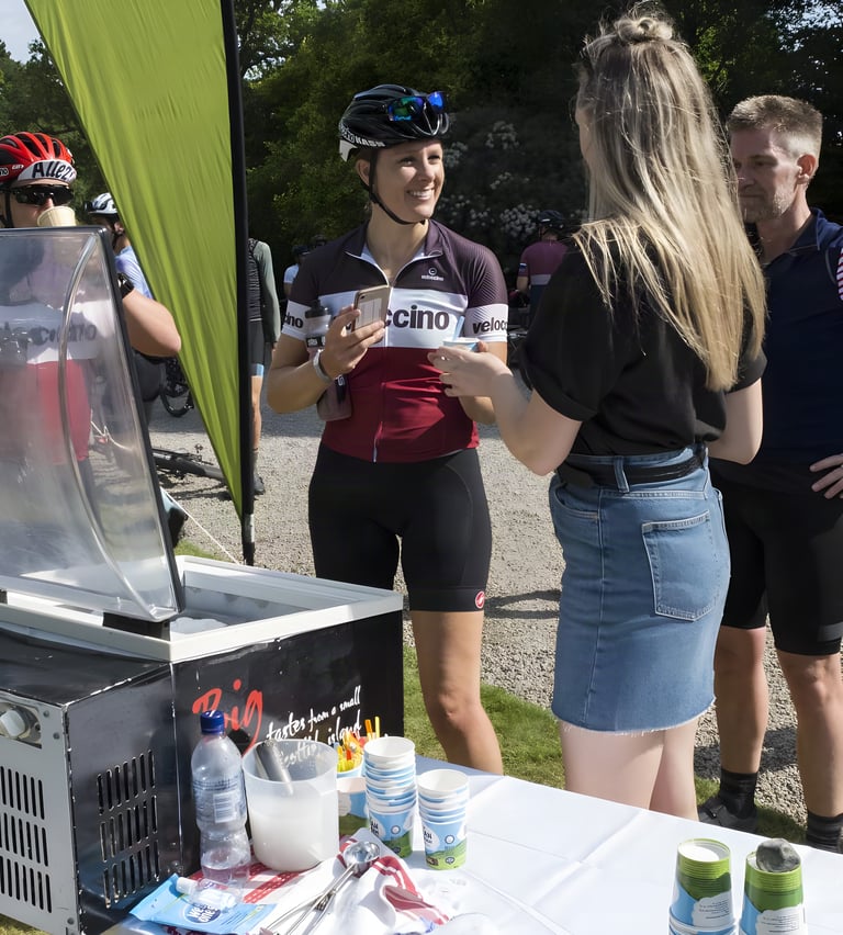 Smiling rider in a cycling jersey is handed a tub of local ice cream at a Grinduro feed station on the Isle of Arran.
