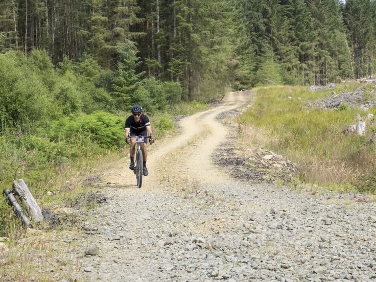Rider on a gravel bike follows a winding forest track of loose stone and sand on the Isle of Arran during Grinduro.