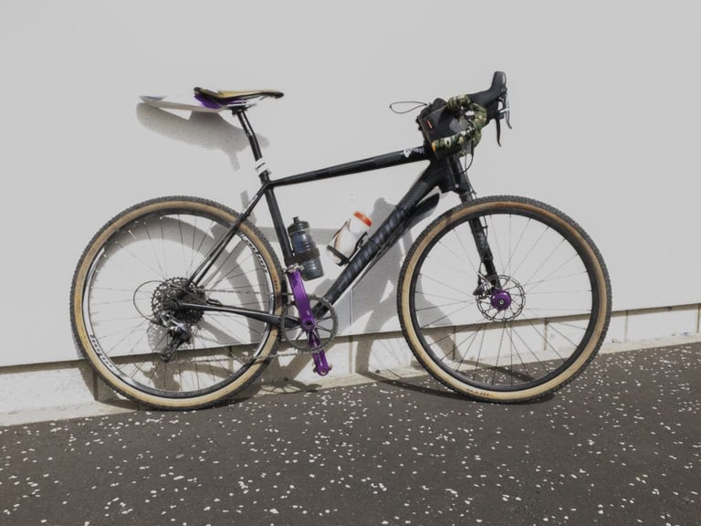 Cannondale Slate with Lefty fork, tan-wall 650b WTB tyres, purple crank and camouflage bar tape against a white wall.