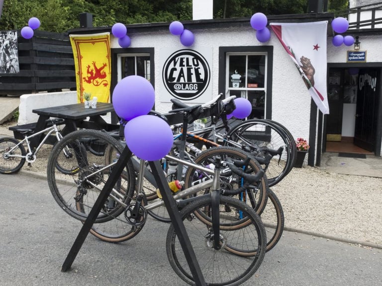 Gravel bikes racked outside Velo Cafe at Lagg, decorated with purple balloons and Scottish and Californian flags.