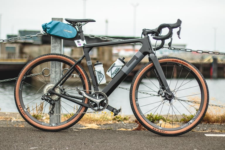 3T Exploro LTD in black with WTB Byway tan-wall tyres, ENVE wheels and a teal saddle bag, side view by the harbour.