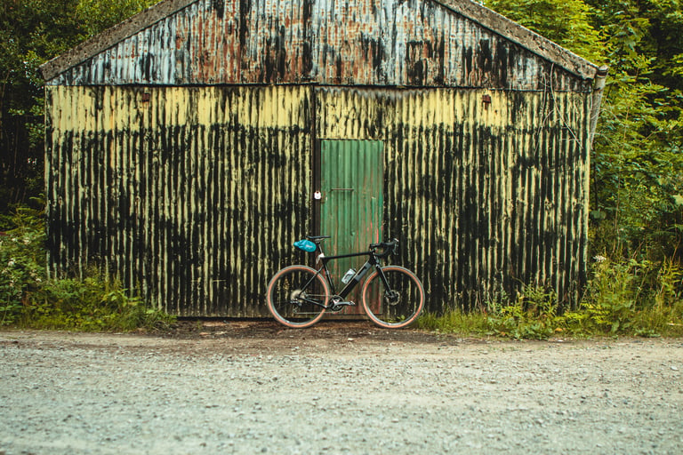3T Exploro leaning against a weathered yellow corrugated shed with a green door beside a gravel track.