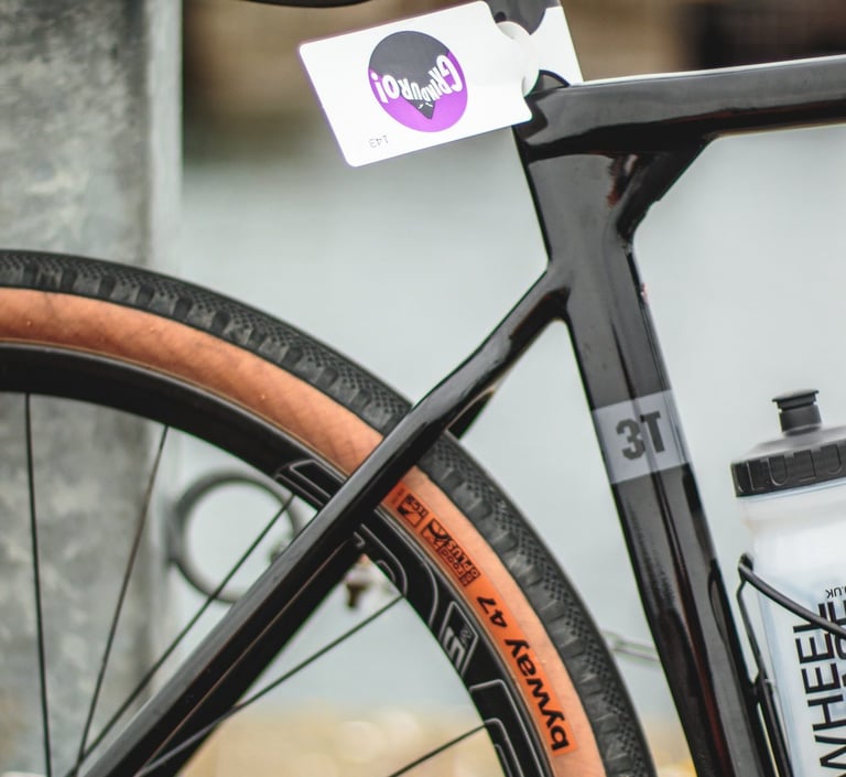Close-up of the 3T Exploro seat stays and 3T logo, with a WTB Byway 47 tan-wall tyre and a Grinduro rider tag.