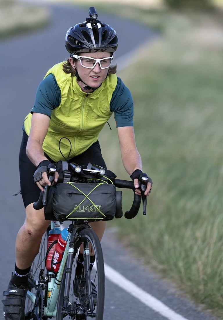 Close-up of Ede Harrison riding her Wolfson with an Alpkit handlebar bag, front light and number 179 on her helmet.