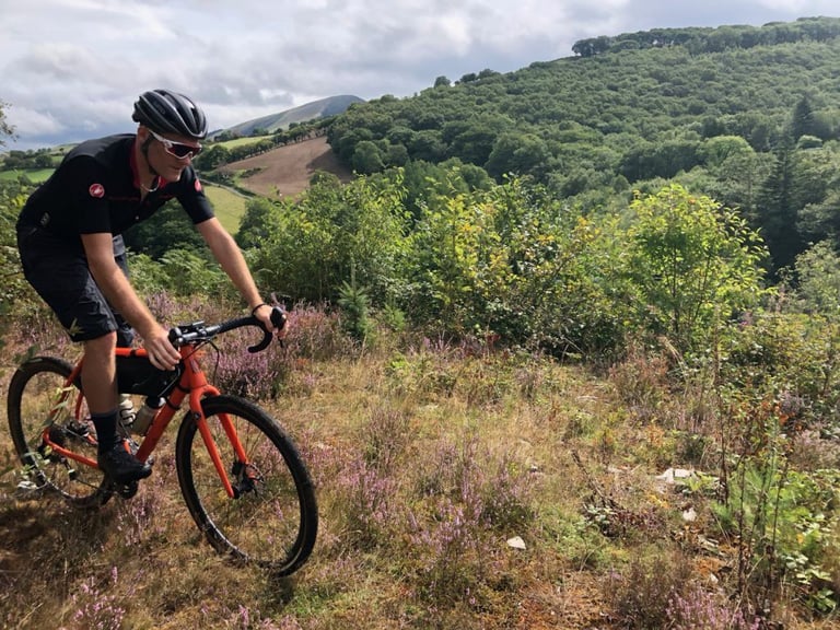 Gravel rider on an orange bike rides through heather on a Bike Corris guided ride in the Dyfi Forest.
