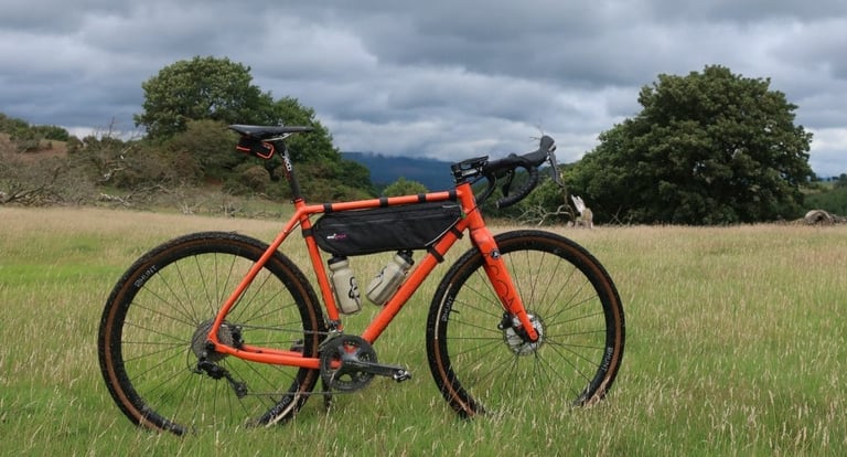Miss Grape Internode frame bag fitted to an orange Mason Bokeh gravel bike in a grassy field.