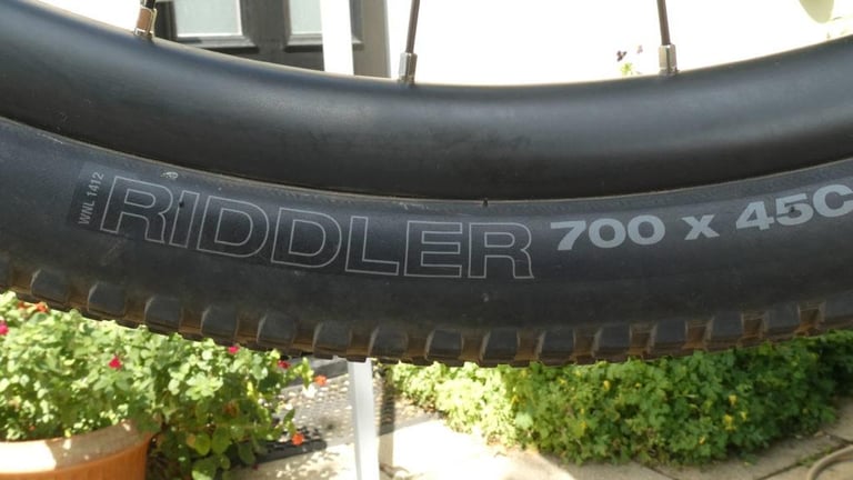WTB Riddler 700 x 45c gravel tyre sidewall with the model name and size printed on it, wheel held up in a garden.