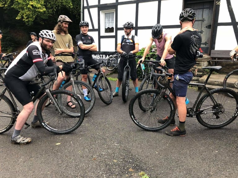 Riders in helmets chat with their Bombtrack bikes outside a half-timbered house at the Groundwork event in Germany.