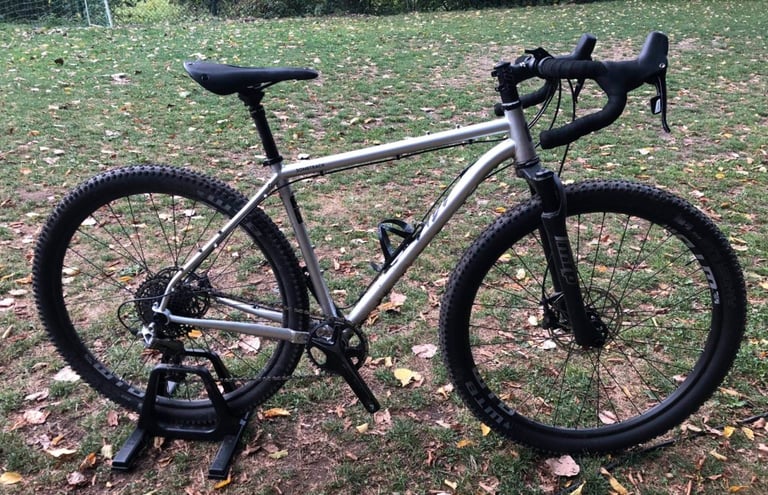 Bombtrack Hook ADV in metallic grey propped on a stand on a leaf-strewn lawn, drop bars and dropper post fitted.