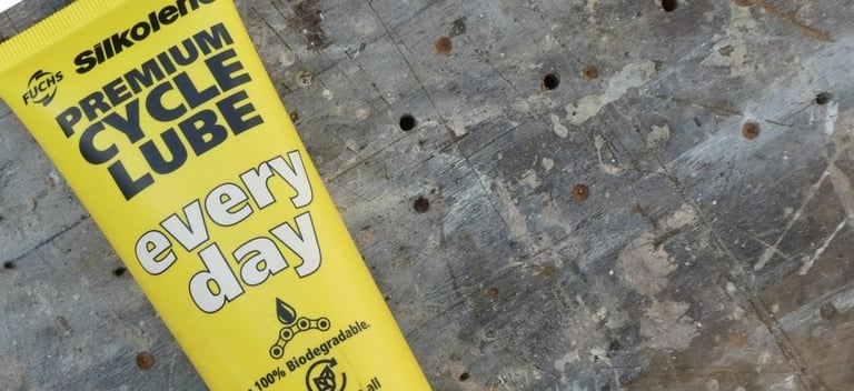 Close-up of the Silkolene Every Day lube tube label, marked 100% biodegradable, on scuffed wood.
