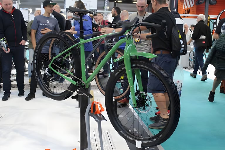 Green Mason ISO with mudguards and big knobbly tyres on a display stand at the Cycle Show as visitors crowd round.