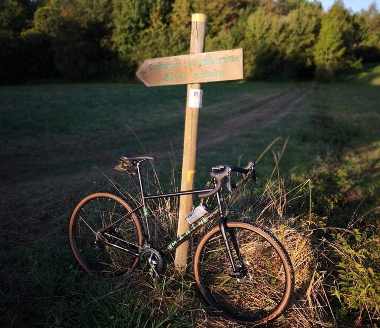 Marin Four Corners propped against a wooden signpost on a grassy track, with a bottle in the cage.